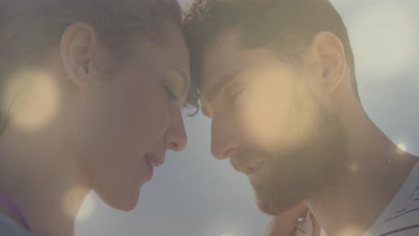 animation of lens flare over caucasian couple embracing and touching head to head on beach