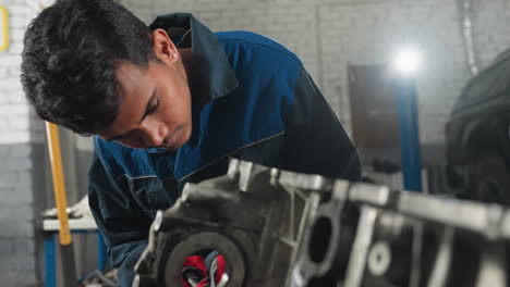 ingeniero de reparación centrado en el trabajo del motor en el taller de automóviles con vista parcial de un colega que le muestra algo, rodeado de herramientas mecánicas