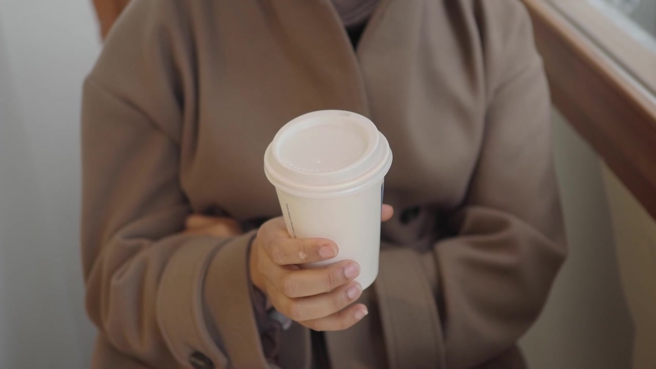 Primo piano di una persona che tiene una tazza di caffè usa e getta bianca