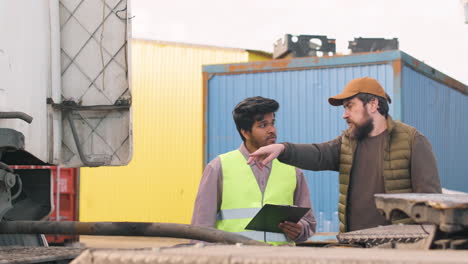 caucasian boss and indian worker organizing a truck fleet in a logistics park while they consulting a document