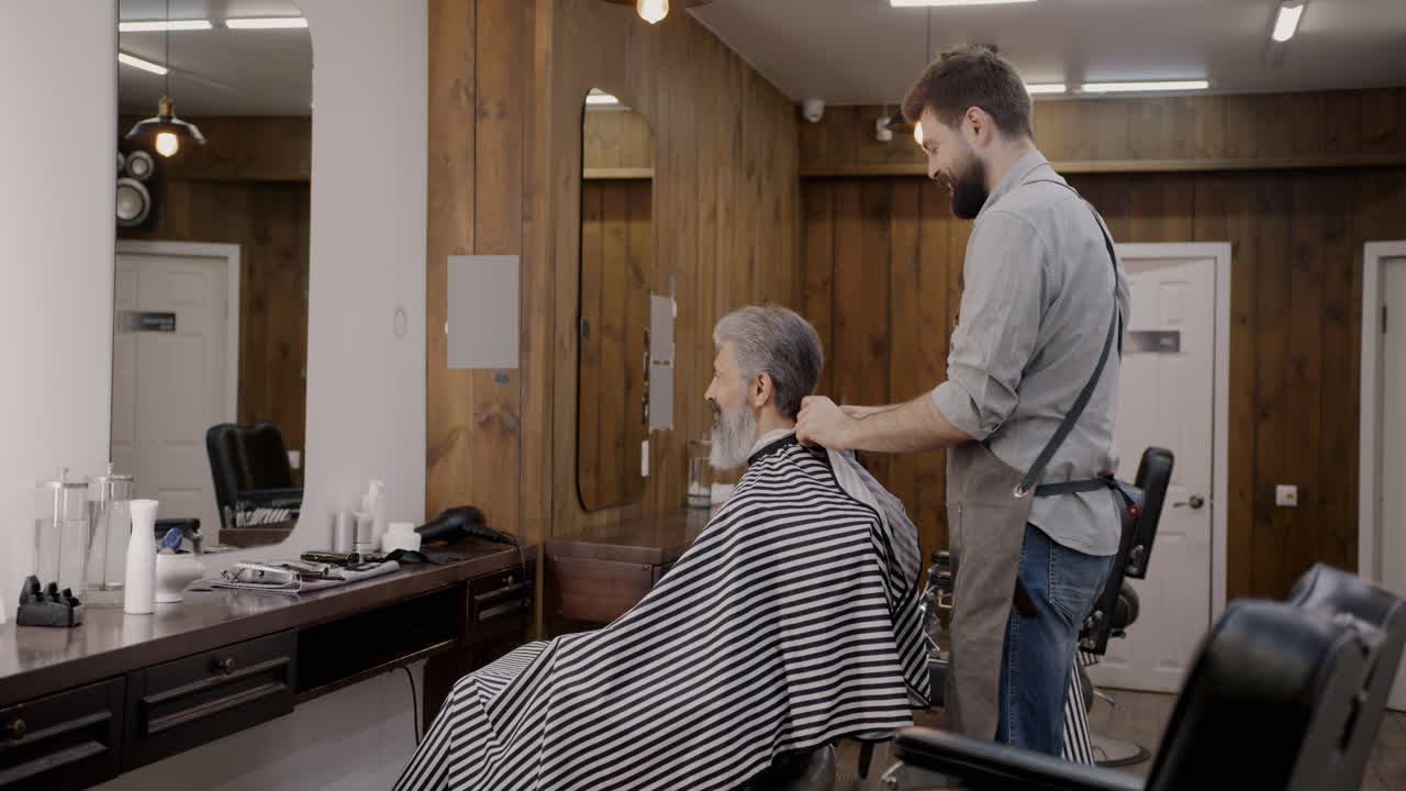 Barbiere che taglia i capelli a un uomo anziano in un moderno negozio da barbiere