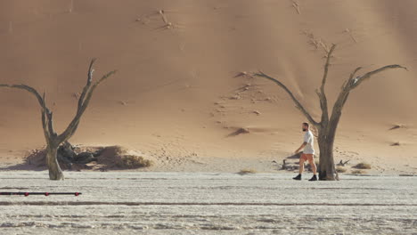 young man with camera walking in the deadvlei, clay pan with dead camelthorn trees near sossusvlei