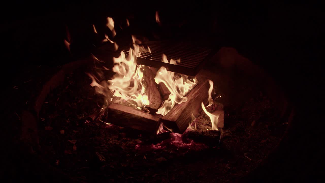 큰 오렌지색 불꽃 캠프불은 철 요리 그릴 아래 로그를 태운다, 밤