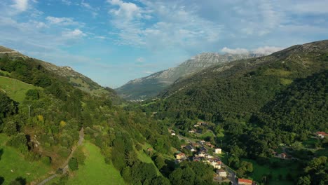 flight in a valley descending in a town with its rural houses slopes of green meadows and forests with a background of a mountain of limestone rocks with a blue sky with clouds cantabria-spain