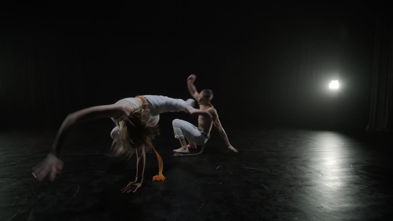 un grupo de bailarines profesionales están practicando capoeira en la oscuridad contra un foco de luz en un fondo negro de estudio. arte marcial afro-brasileño que combina elementos de la danza.