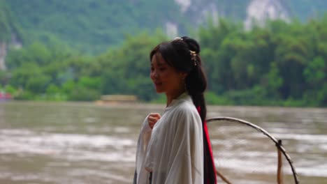 joven con ropa tradicional hanfu se equilibra en una balsa de bambú a lo largo del río li, china