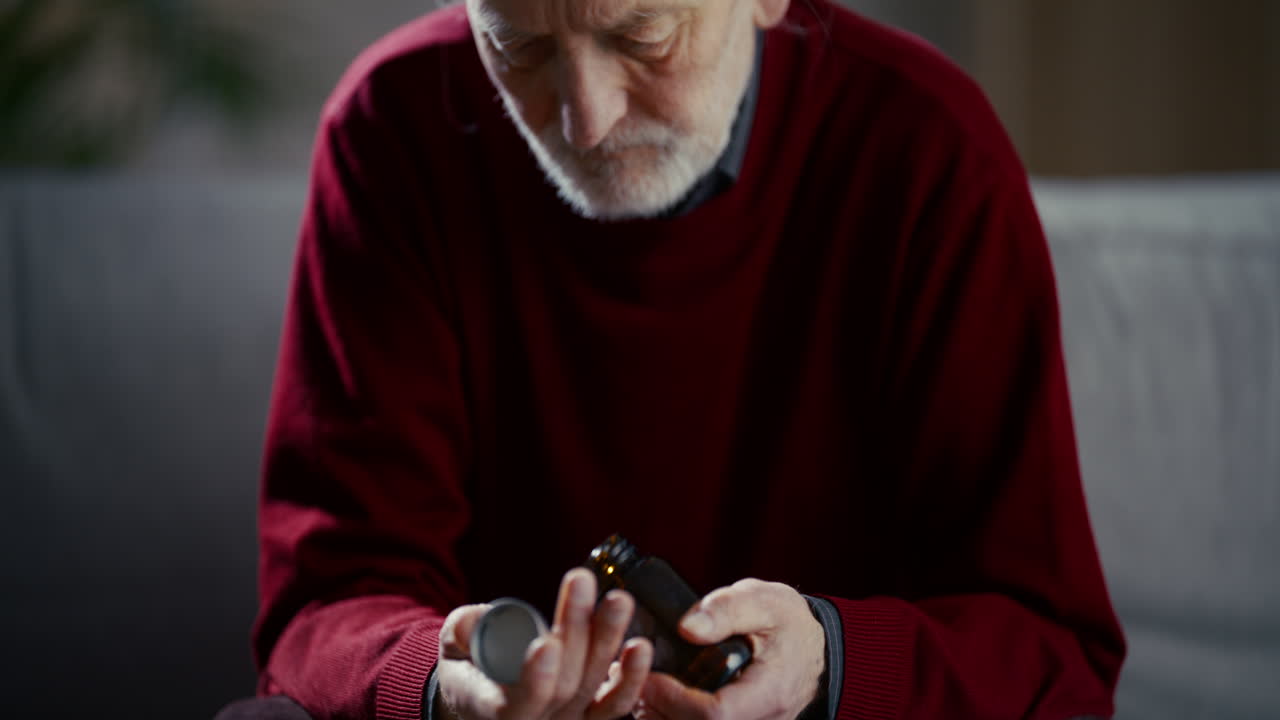 Elderly Man Opening a Pill Bottle and Looking Sad