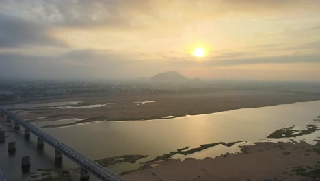 aerial drone shot of vijayawada in the tranquil early hours, with sunlight piercing through the morning clouds to reveal the city.