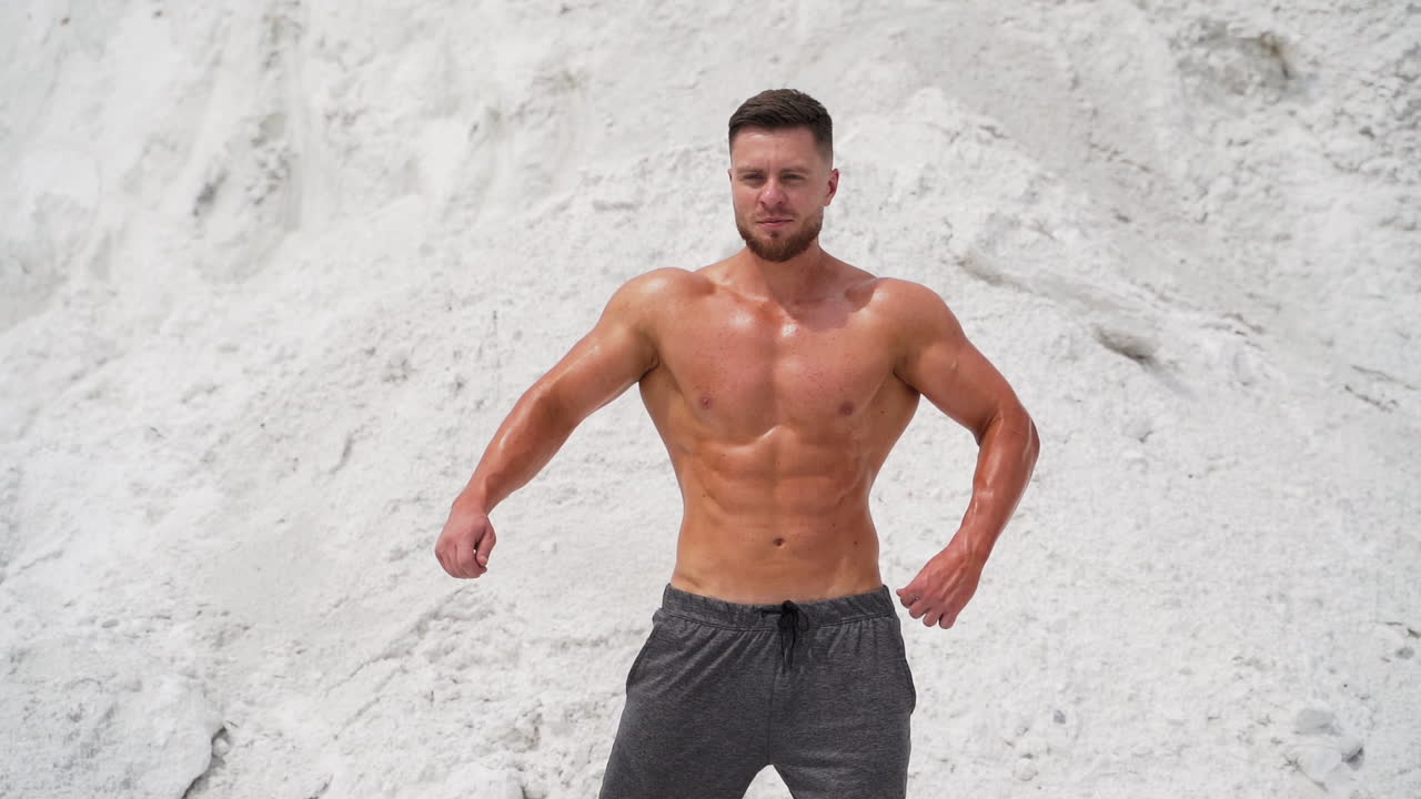 Spots man standing in pose. Well built bodybuilder posing in the mountains