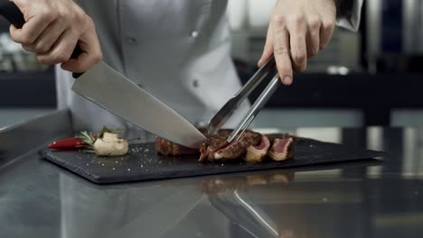 Chef-hands-cutting-steak-at-kitchen-restaurant.-Closeup-chef-slicing-meat