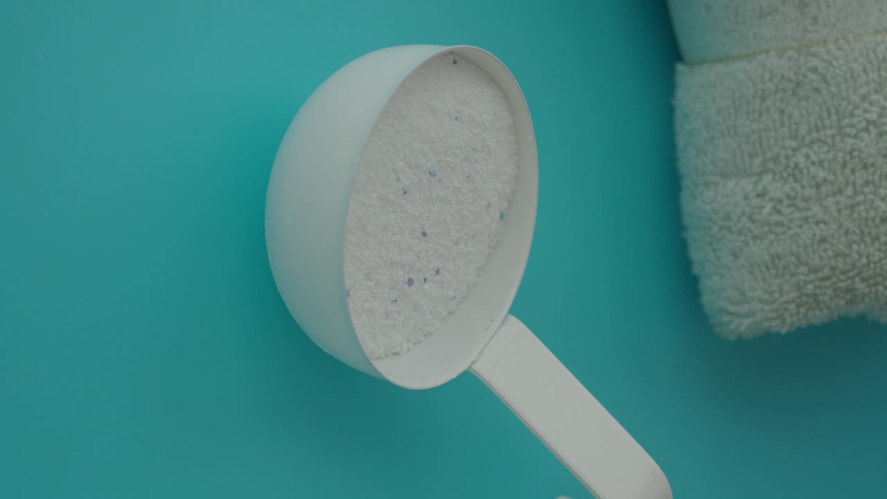 Washing Powder in Scoop with Towel on Turquoise Background