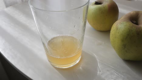 fresh natural cider pouring into a glass, with apples in the background