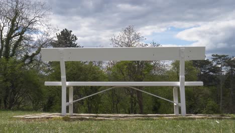 a lonely white bench in an empty park during daytime - wide shot