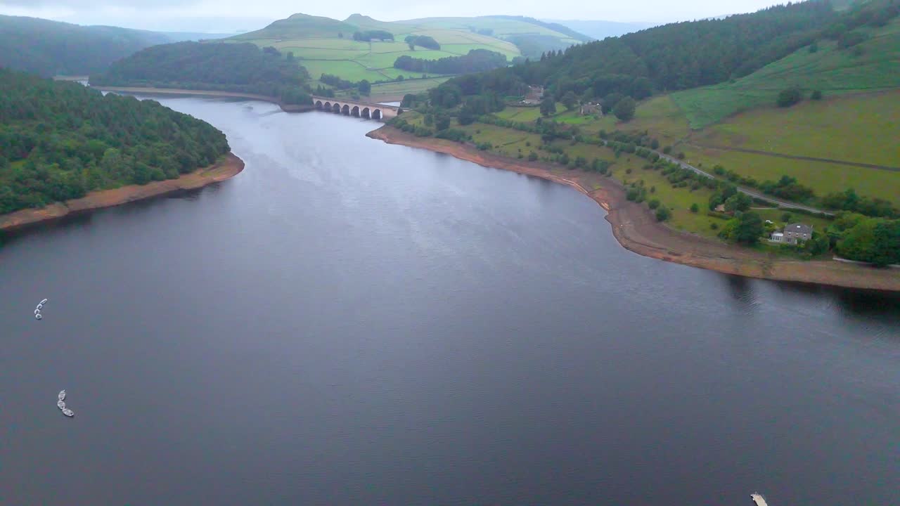 Drone camera glides above a wide reservoir, revealing a bridge, green hills, and a rural landscape under soft daylight with smooth, steady movement
