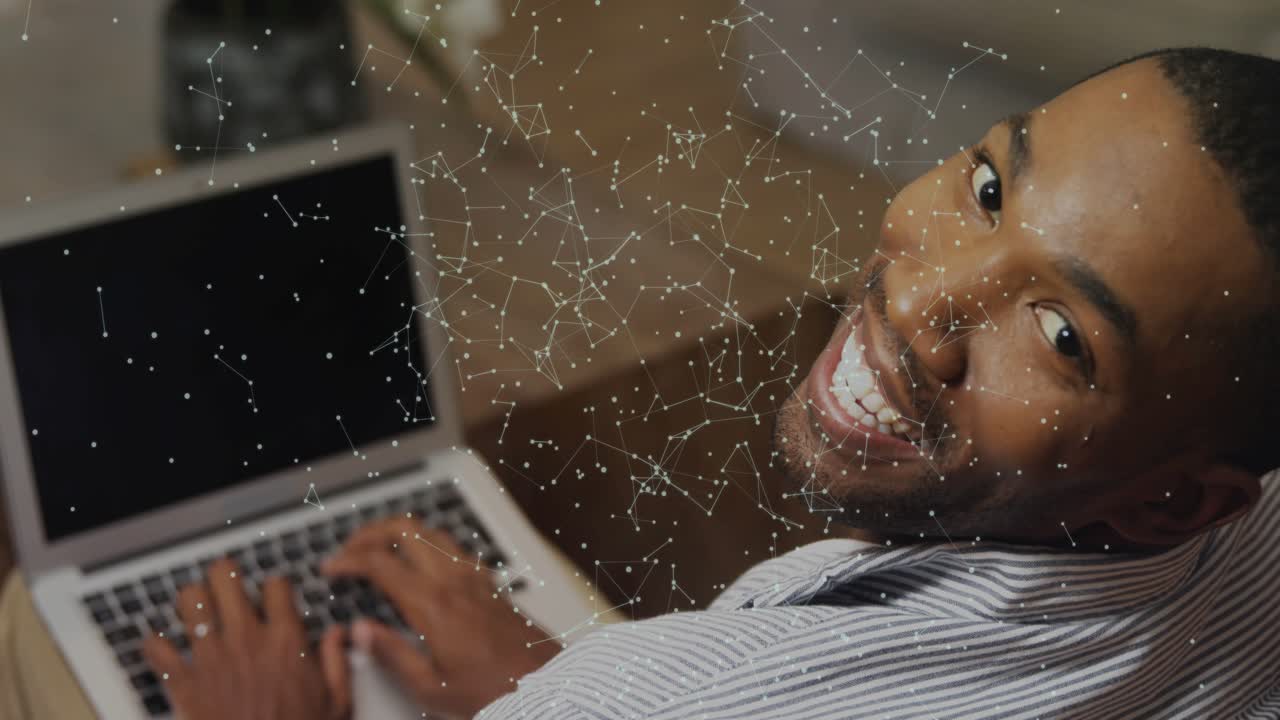 Man typing on laptop pausing turning head smiling as constellation overlay showing network concept