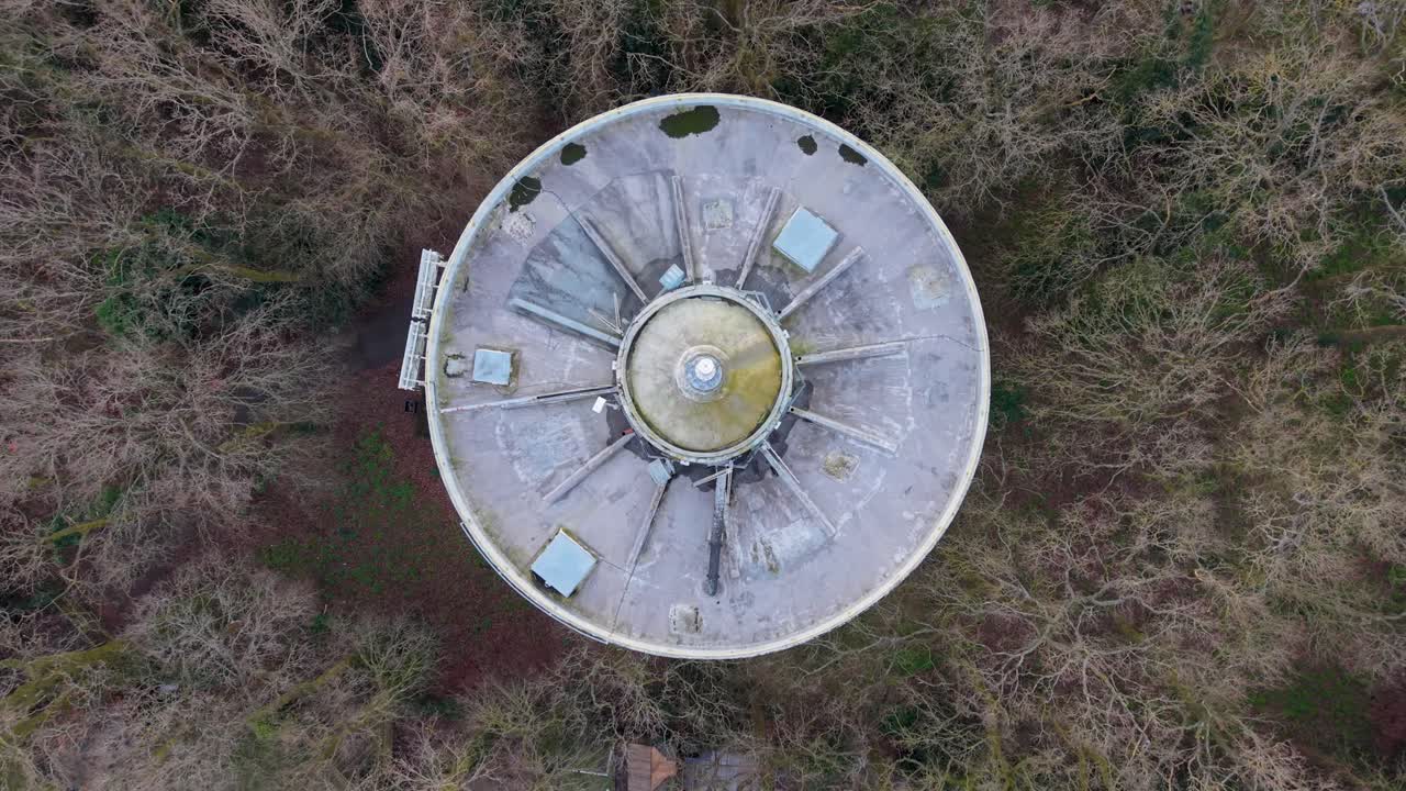 Bengeo water tower drone ascent, top-down view of circular reservoir roof surrounded by winter woodland, revealing urban infrastructure and geometric patterns from above