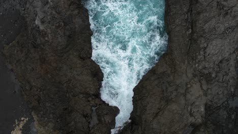 Top-Down-View-Over-A-Volcanic-Rocky-Shoreline-With-Foaming-Blue-Waves-Splashing