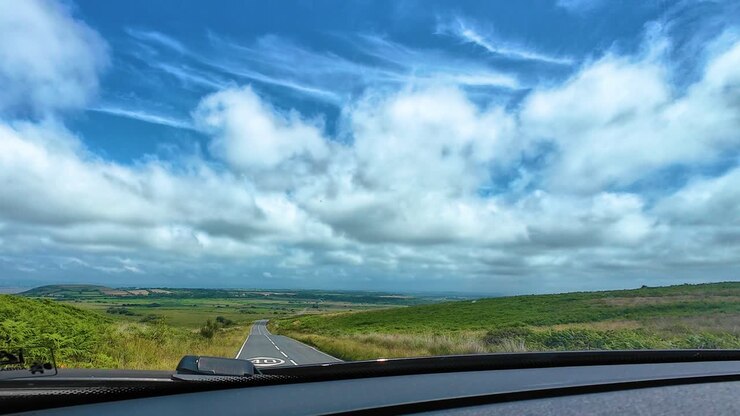 Dashcam View of Welsh Countryside as Car Moves Around Sharp Corner to Reveal Incredible Straight Road Over Gower Pensinsula with Dynamic Sky. Transport Travel Footage