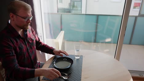 el hombre caucásico se sienta a la mesa con un plato vacío y un vaso de agua