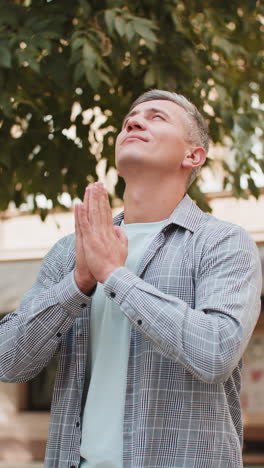 caucasian mature man tourist praying with closed eyes to god asking for blessing on city town street