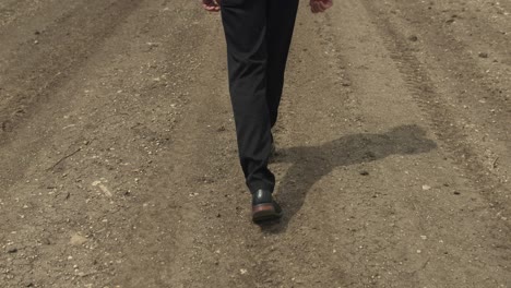 feet of man walking on dirt road by expansive fields