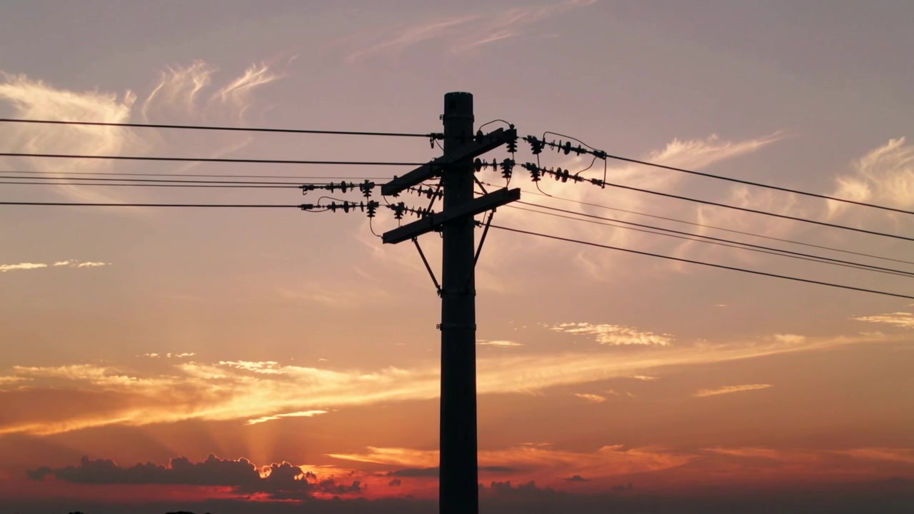 夕日が田園の地平線を照らし、電柱、碍子、電線がシルエットとして浮かび上がっている。
