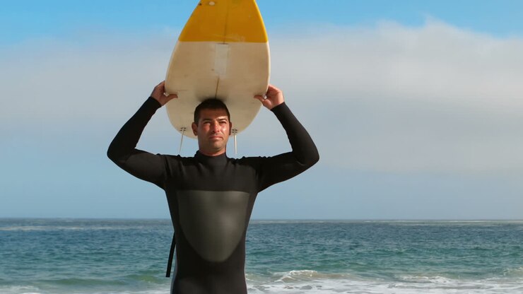 Uomo in muta che tiene la tavola da surf sopra la testa
