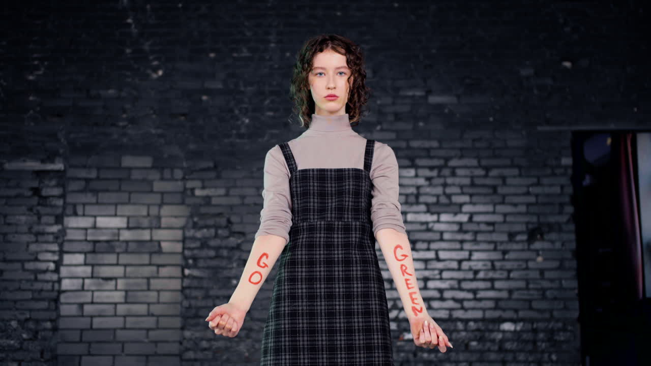 серьезная молодая активистка экологического движения смотрит в камеру и показывает руки с надписью go green".