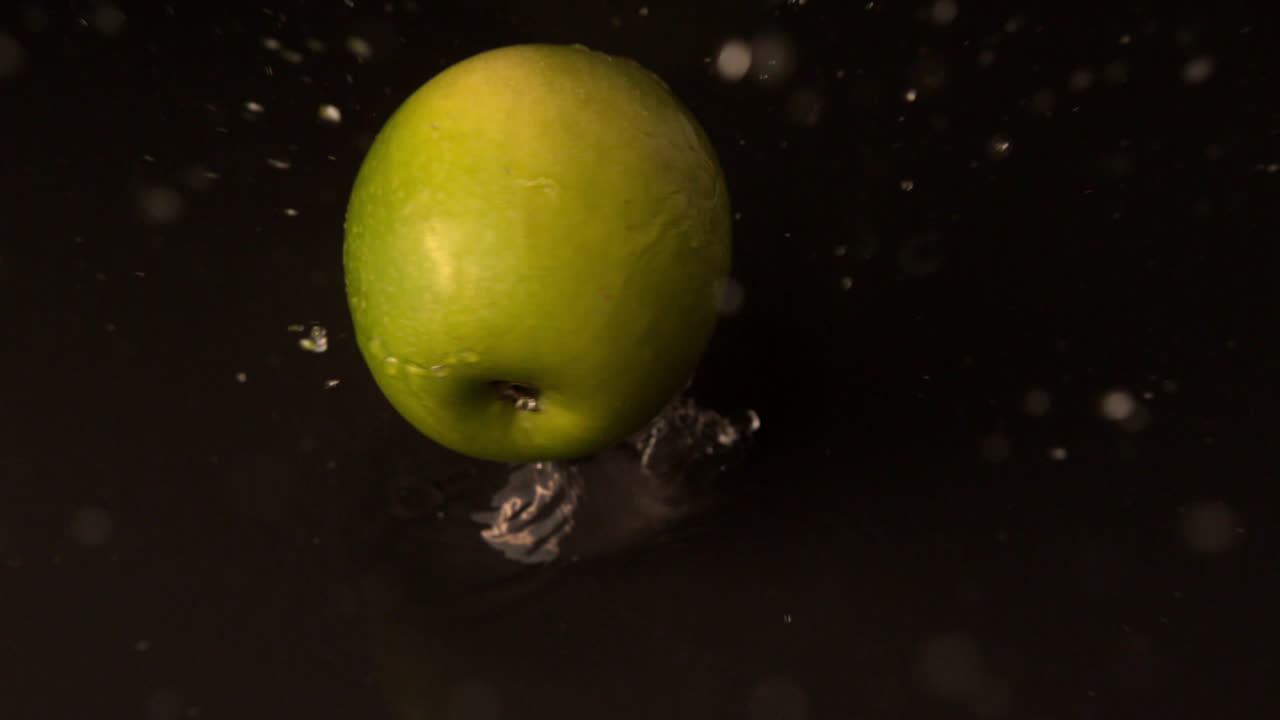 Mela verde che cade su una superficie nera bagnata