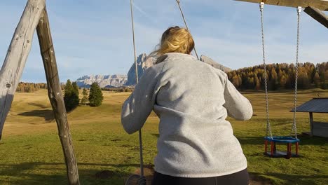 Rear-view-of-woman-kicking-legs-out-as-she-swings-in-the-countryside-admiring-the-Dolomites