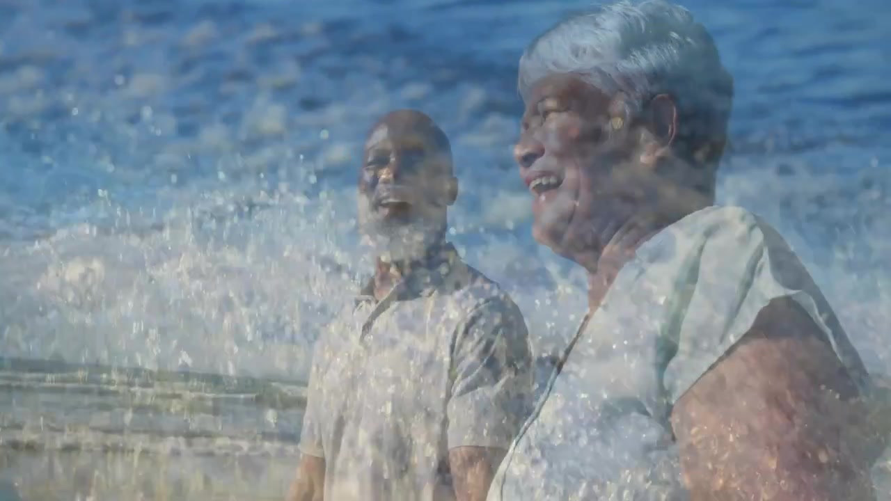 Coppia in viaggio passeggia sulla riva, la donna indica il mare, l'uomo segue il suo sguardo, condividendo la vista, mentre le onde si infrangono.