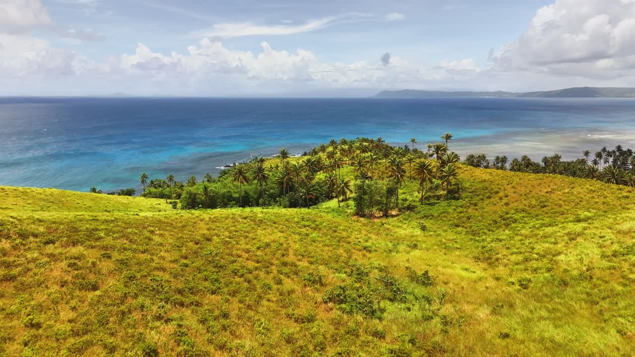 Dolci colline verdi conducono a una penisola coperta di palme circondata dall'oceano turchese, con cieli sereni sopra e isole lontane all'orizzonte sull'isola di Corregidor, Isole Siargao, Filippine.