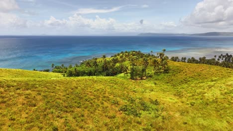 rolling green hills lead to a palm-covered peninsula surrounded by turquoise ocean, with clear skies above and distant islands on the horizon on corregidor island, siargao islands, philippines