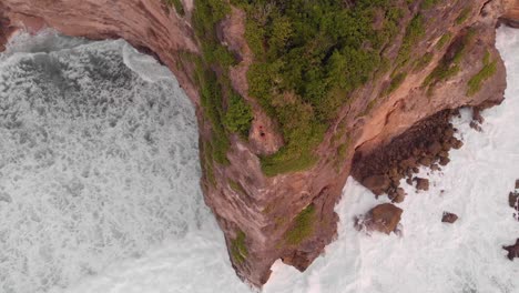 Toma-Aérea-Cinematográfica-Suave-De-Grandes-Olas-Que-Se-Estrellan-Contra-El-Borde-De-Un-Enorme-Acantilado-En-Uuwatu,-Bali-Durante-La-Hora-Dorada-En-La-Puesta-De-Sol-De-Verano-1