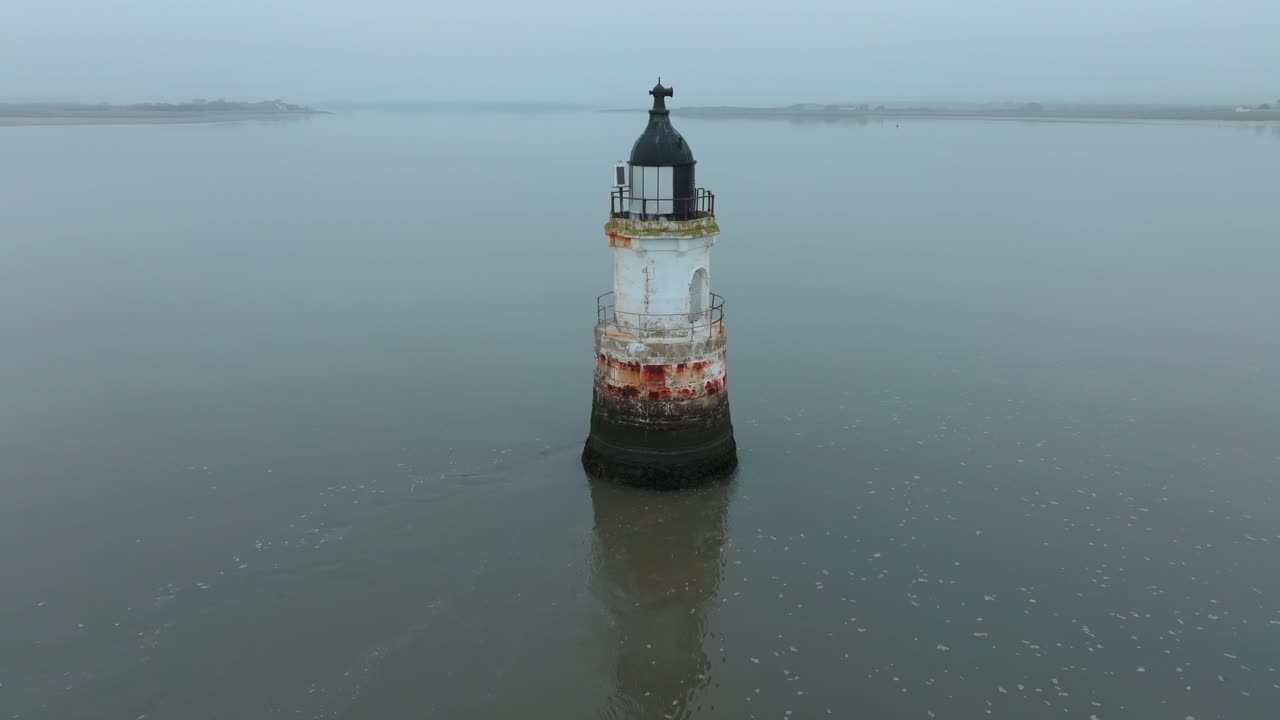 Flashing Light On Rusty Derelict Lighthouse On A Misty Evening As Calm Tide Water Passes by. With Misty Coastline. Plover Scar Lighthouse, Lancashire, UK