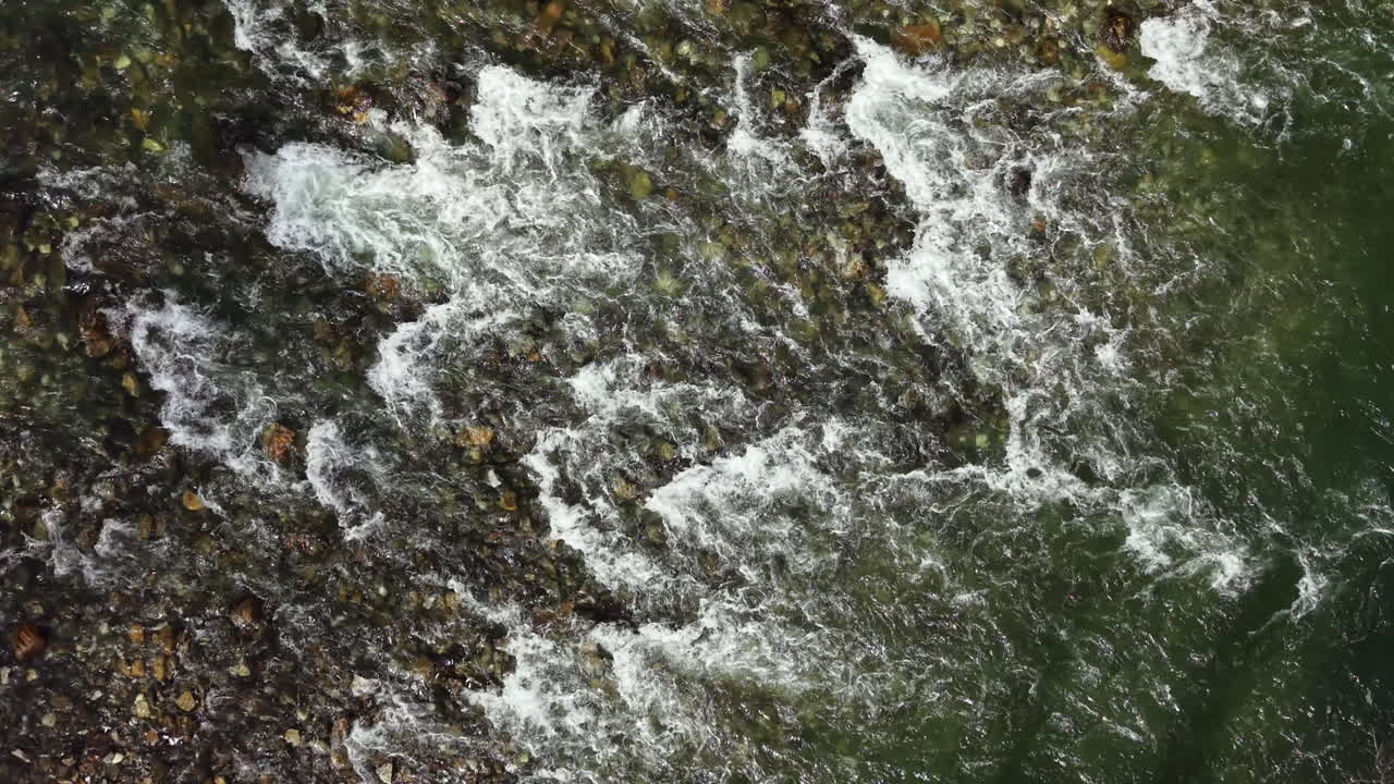 Le onde si infrangono contro la costa rocciosa mentre l'acqua scorre e vortica in una scena costiera di giorno in un ambiente naturale vicino all'oceano