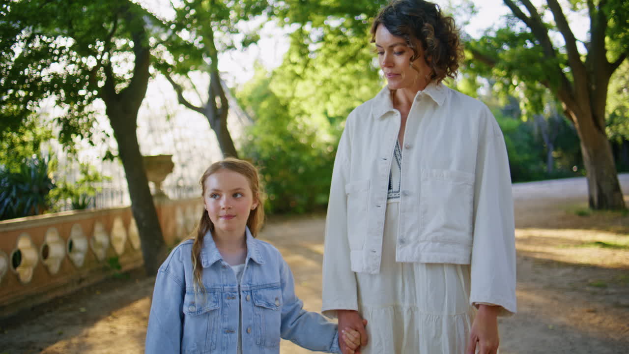 Happy woman walking girl sunny alley at family weekend. Mother daughter going