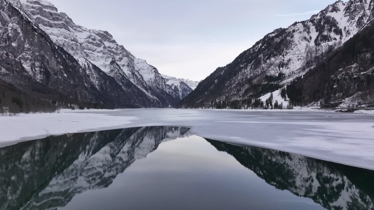 Klöntalersee stunning view in winter, mirror reflection of snow-capped Swiss alps on frozen lake.