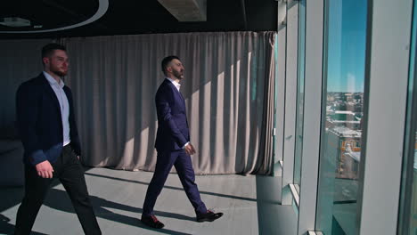 businessmen looking out of large office window. back full-length portraits of three entrepreneurs in costumes standing by the window in a office at daytime. rear view