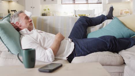 happy caucasian man lying on sofa in living room, sleeping