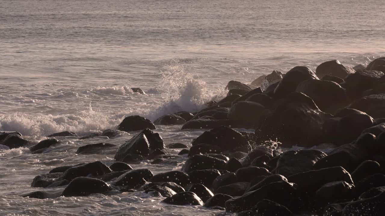 천천히 움직이는 파도가 황금빛 해가 뜨는 아래 바위 위에 부히고 있습니다.