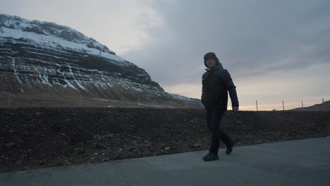 man walk on concrete pavement near huge icelandic mountain during sunset