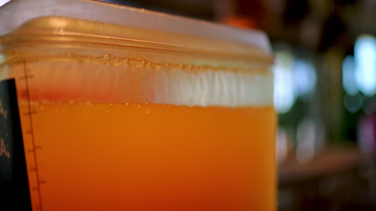 Fresh orange juice pouring into measuring plastic container, revealing vibrant bubbles and foam, creating refreshing citrus beverage with blurred background highlighting natural liquid texture