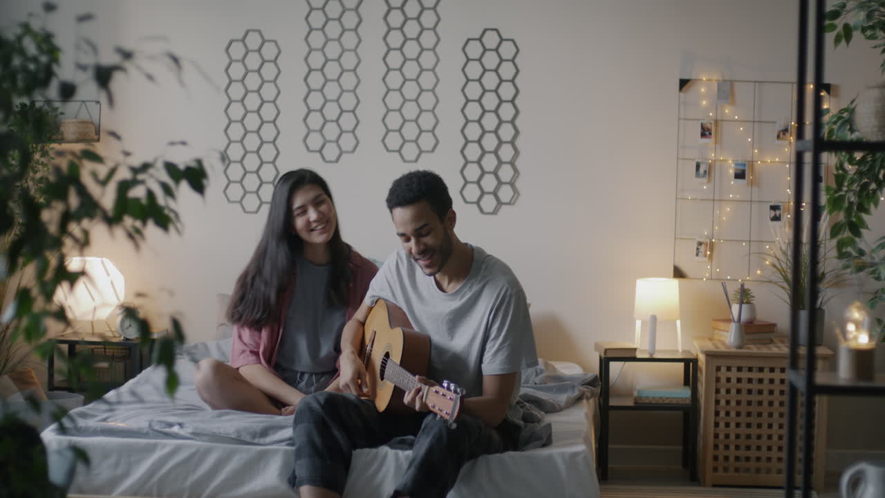 Couple playing guitar in a bedroom