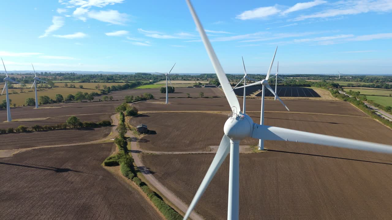 High resolution FPV drone footage of wind turbines generating electricity over solar farm, England
