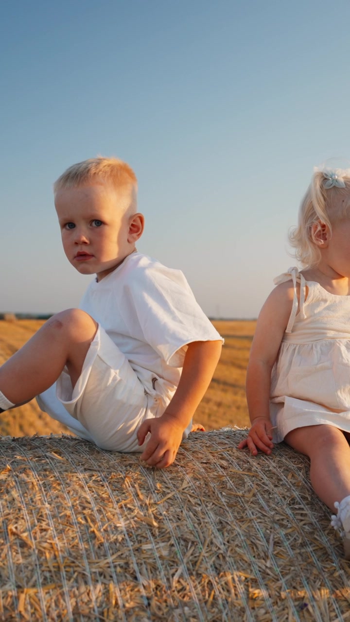 Due bambini piccoli seduti su una balla di fieno in un campo raccolto