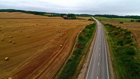 Fahrzeuge-Fahren-Auf-Einer-Langen-Asphaltstraße-Durch-Ackerland-Mit-Heuballenrollen