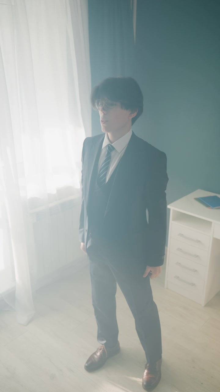 Uomo asiatico che si veste con abito formale e gilet, abbottonandosi la giacca e sistemandosi la cravatta, scarpe lucide su pavimento in legno, rituale di preparazione per un traguardo di carriera, luce naturale dalla finestra e composto, pronto.