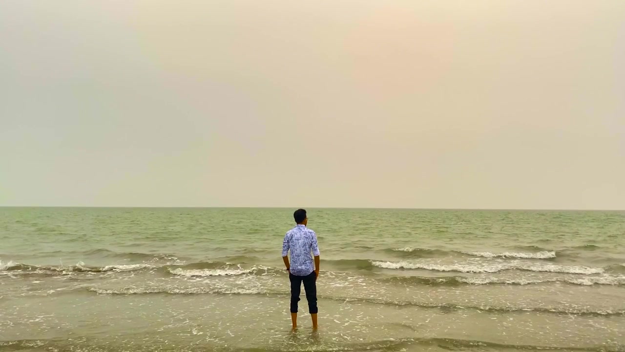 Un uomo solitario in piedi su una spiaggia che si gode la solitudine in riva al mare - Campo lungo