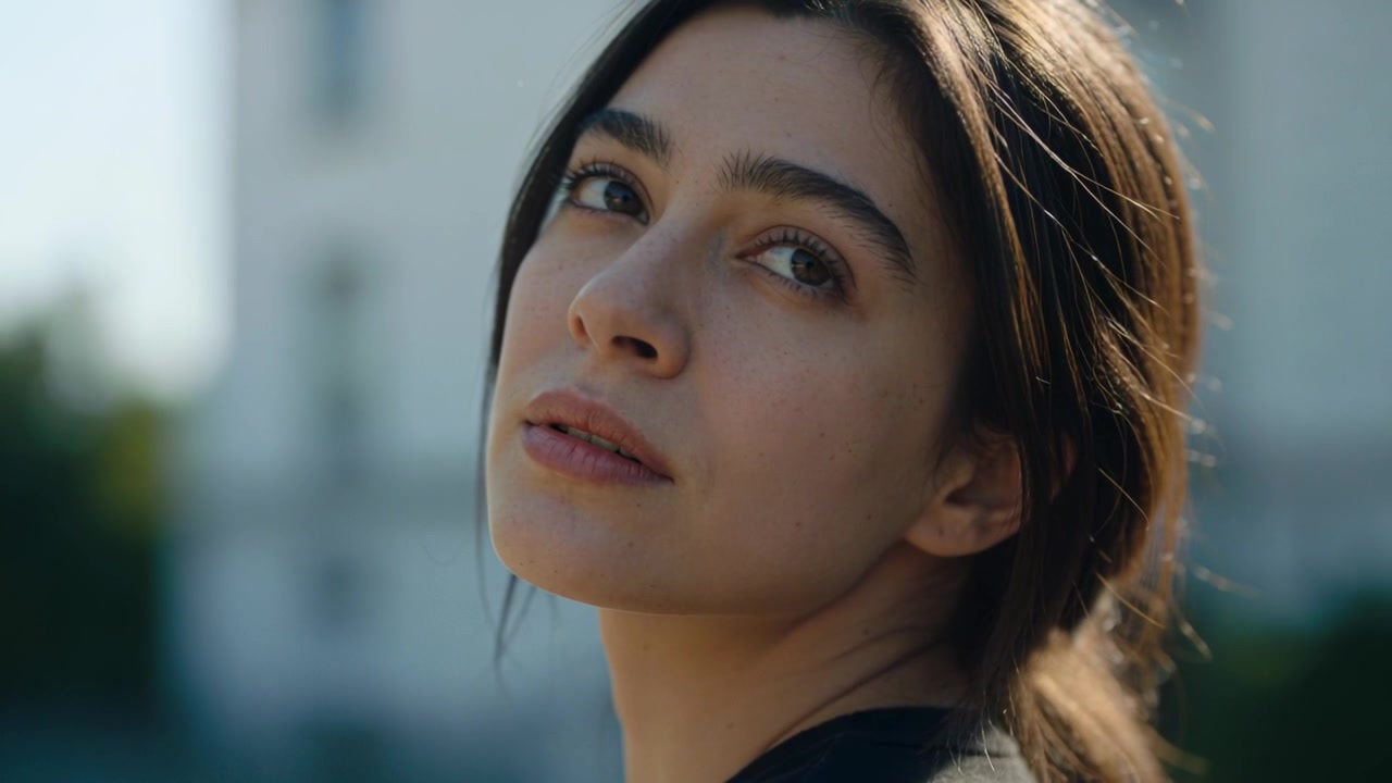 Donna che si gira, alzando e spostando lo sguardo mentre viene filmata per un ritratto vicino a un edificio chiaro con la parte superiore scura